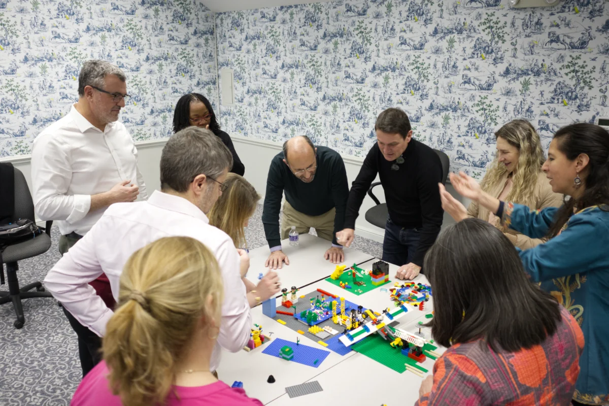 workshop-team-model-building Workshop participants smiling and building together with a variety of LEGO bricks